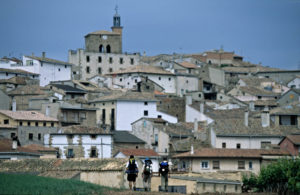 Three pilgrims at the entrance of Cirauqui with the village on the background